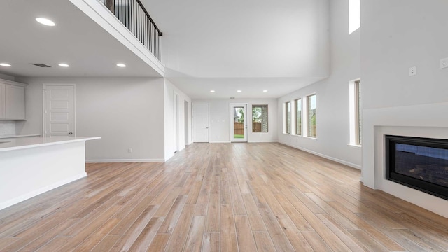 4343 Hudson St, Fate, TX 75087 - unfurnished living room featuring a high ceiling, a glass covered fireplace, light wood-style flooring, and recessed lighting
