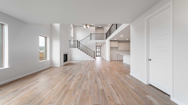 4343 Hudson St, Fate, TX 75087 - unfurnished living room featuring ceiling fan, light wood-type flooring, stairway, a glass covered fireplace, and recessed lighting
