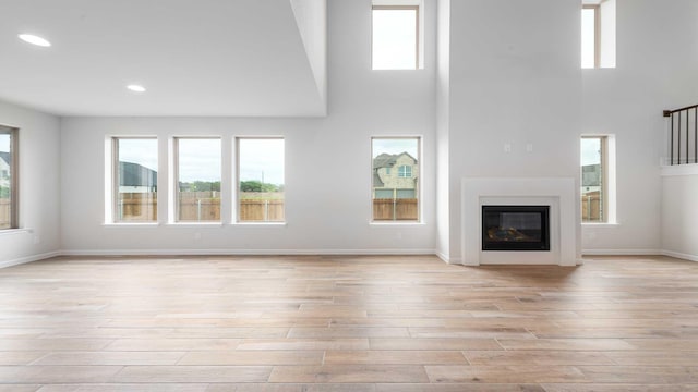 4343 Hudson St, Fate, TX 75087 - unfurnished living room featuring light wood-style flooring, healthy amount of natural light, a high ceiling, a glass covered fireplace, and recessed lighting