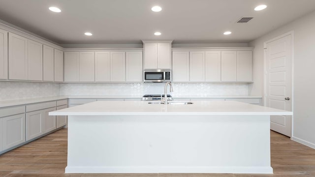 4343 Hudson St, Fate, TX 75087 - kitchen featuring stainless steel microwave, an island with sink, light countertops, light wood-type flooring, and recessed lighting