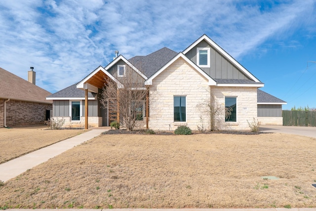 view of front of property with stone siding, board and batten siding, fence, and roof with shingles