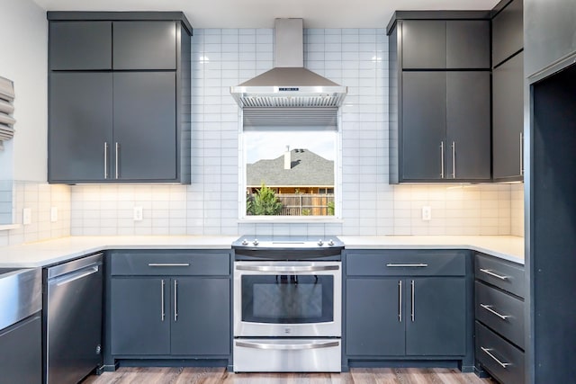 kitchen featuring light countertops, wall chimney range hood, wood finished floors, and appliances with stainless steel finishes