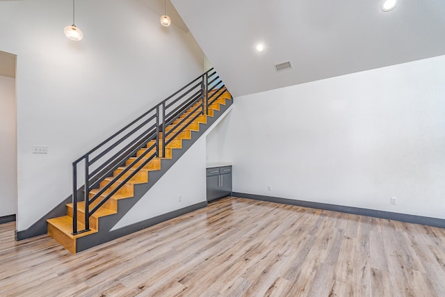 stairs with a high ceiling, wood finished floors, visible vents, and baseboards