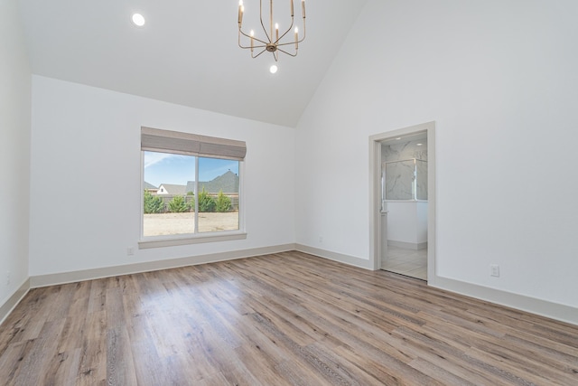 spare room with recessed lighting, an inviting chandelier, wood finished floors, high vaulted ceiling, and baseboards