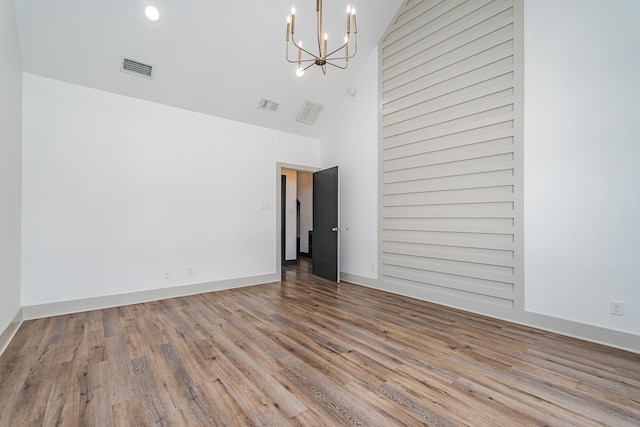 empty room featuring a high ceiling, wood finished floors, visible vents, and an inviting chandelier