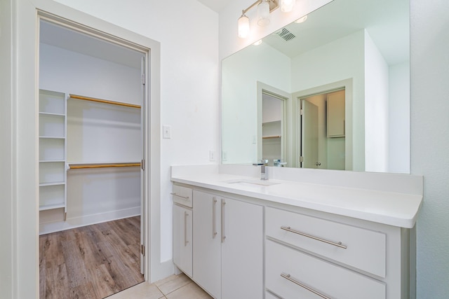 bathroom with a walk in closet, visible vents, vanity, tile patterned flooring, and baseboards