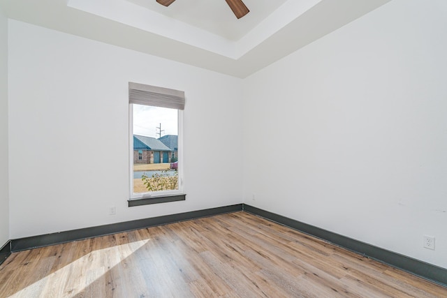 empty room with a ceiling fan, a tray ceiling, baseboards, and wood finished floors