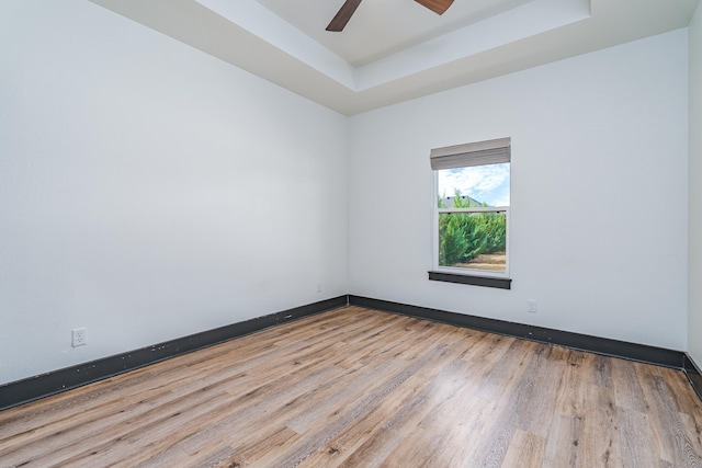 empty room featuring ceiling fan, wood finished floors, a raised ceiling, and baseboards