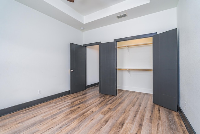 unfurnished bedroom featuring wood finished floors, visible vents, baseboards, a closet, and a raised ceiling