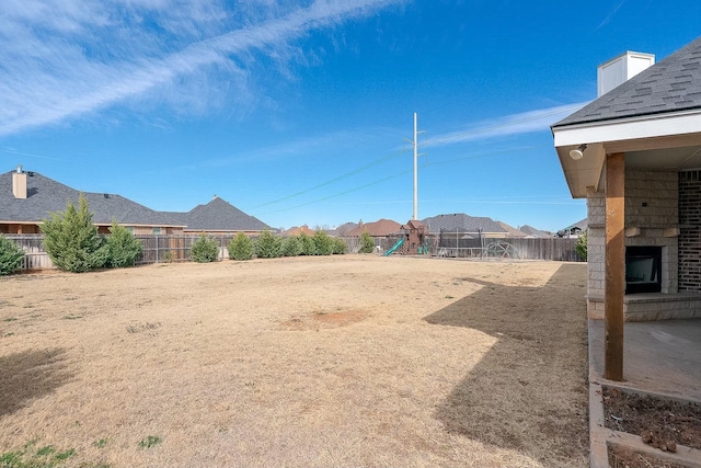 view of yard featuring an outdoor brick fireplace, a playground, and a fenced backyard