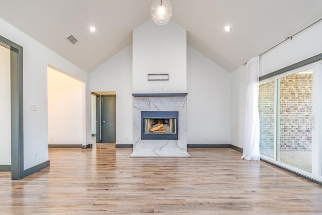 unfurnished living room with light wood finished floors, visible vents, a high end fireplace, high vaulted ceiling, and baseboards