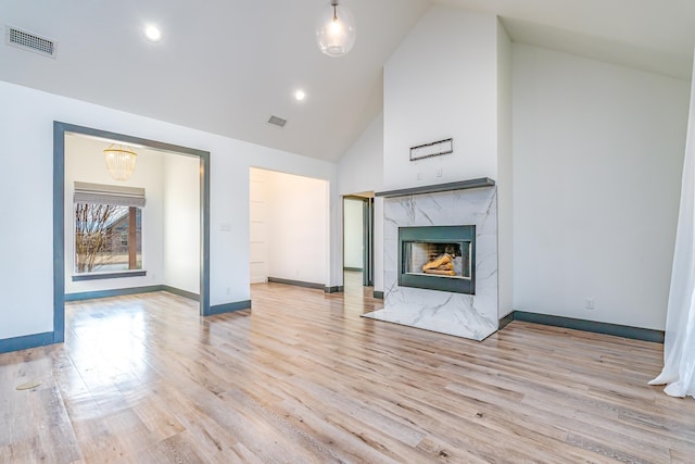 unfurnished living room with baseboards, visible vents, a premium fireplace, wood finished floors, and high vaulted ceiling