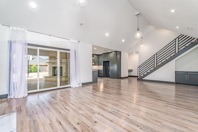 unfurnished living room featuring stairs, high vaulted ceiling, light wood finished floors, and baseboards