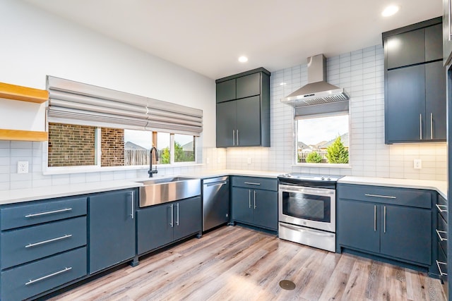 kitchen featuring tasteful backsplash, light countertops, light wood-style flooring, appliances with stainless steel finishes, and wall chimney exhaust hood