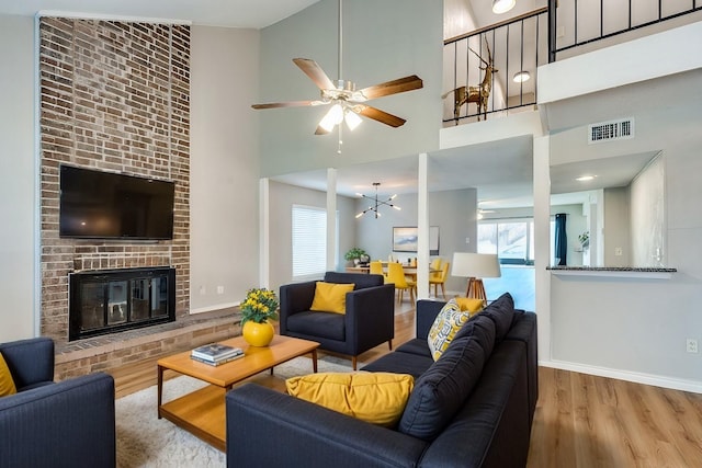 living area featuring visible vents, ceiling fan with notable chandelier, wood finished floors, a fireplace, and baseboards