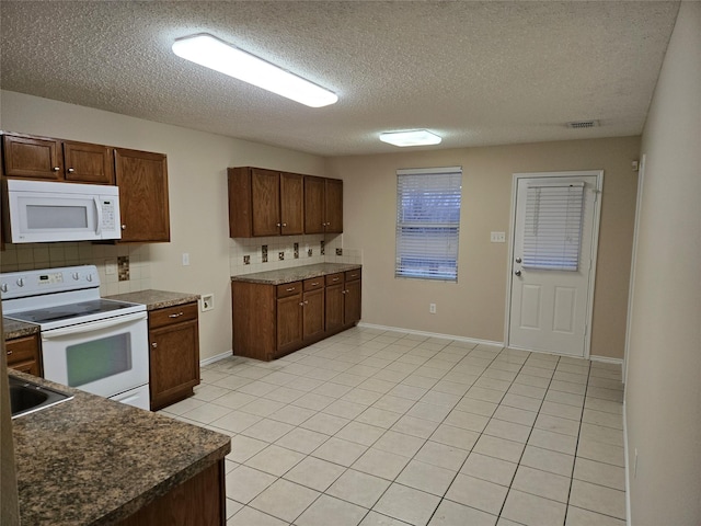 kitchen with tasteful backsplash, dark countertops, white appliances, and light tile patterned floors