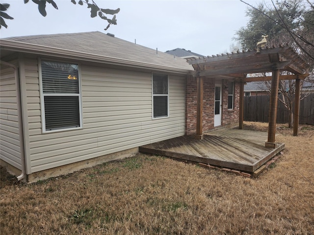 rear view of house featuring a lawn, fence, a deck, a pergola, and brick siding