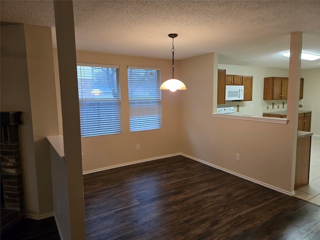 unfurnished dining area featuring baseboards, dark wood finished floors, and a textured ceiling