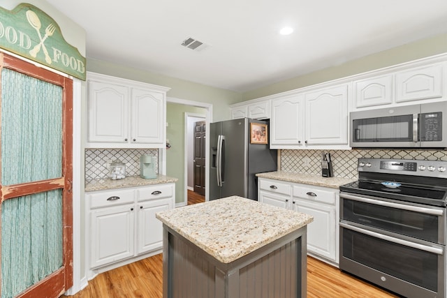 kitchen featuring tasteful backsplash, visible vents, white cabinets, stainless steel appliances, and light wood-style floors