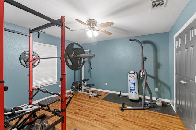 exercise area featuring baseboards, visible vents, a ceiling fan, wood finished floors, and a textured ceiling