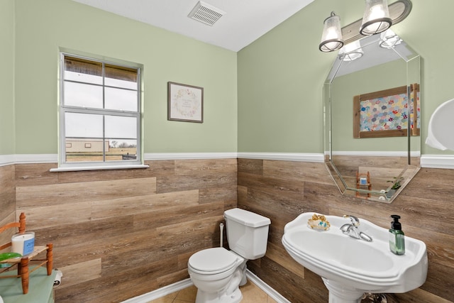 bathroom featuring tile walls, visible vents, toilet, wainscoting, and a sink