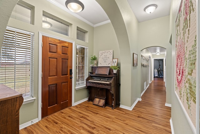 foyer with arched walkways, crown molding, baseboards, and wood finished floors