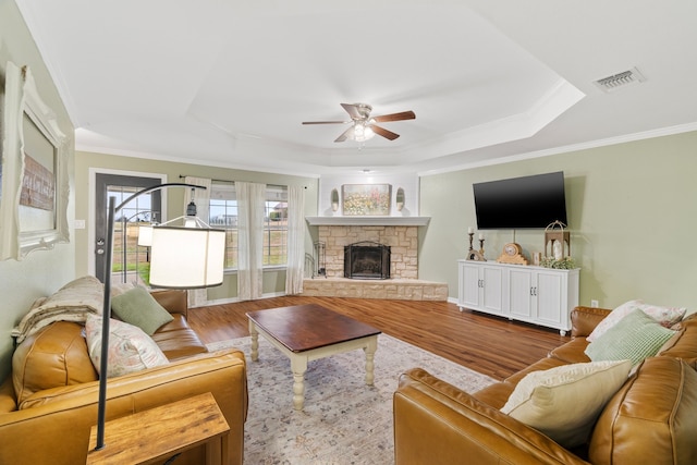 living room with visible vents, a raised ceiling, a ceiling fan, wood finished floors, and a stone fireplace