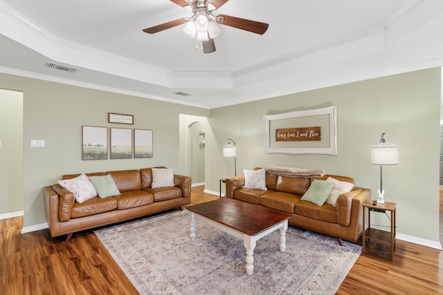 living room with a tray ceiling, visible vents, crown molding, and wood finished floors