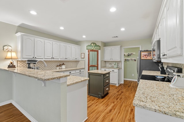 kitchen with light wood-style flooring, stainless steel appliances, a peninsula, visible vents, and white cabinetry