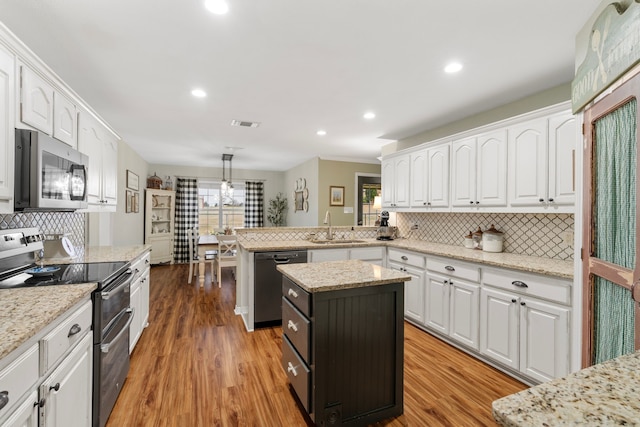 kitchen with stainless steel appliances, a peninsula, a sink, light wood-style floors, and white cabinets