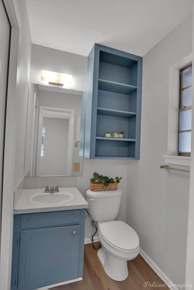 half bathroom with toilet, vanity, wood finished floors, plenty of natural light, and baseboards