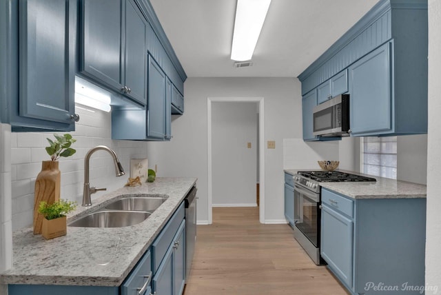 kitchen featuring light wood-style flooring, light stone countertops, stainless steel appliances, blue cabinetry, and a sink