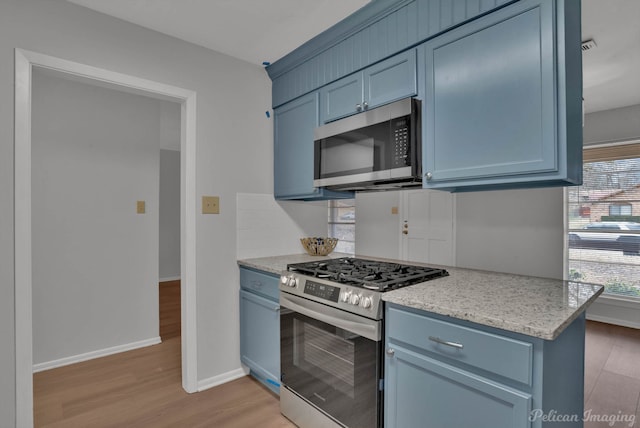 kitchen with baseboards, stainless steel appliances, light wood-type flooring, blue cabinetry, and backsplash