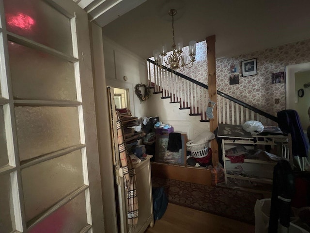 staircase featuring wallpapered walls, wood finished floors, and an inviting chandelier