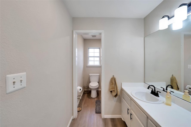 bathroom featuring toilet, baseboards, wood finished floors, and vanity