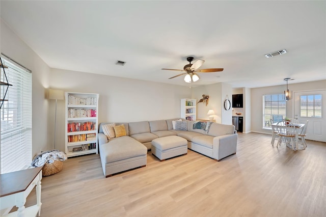 living area featuring light wood-style floors, ceiling fan, and visible vents