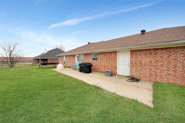 rear view of property with brick siding, a yard, a shingled roof, a patio area, and fence