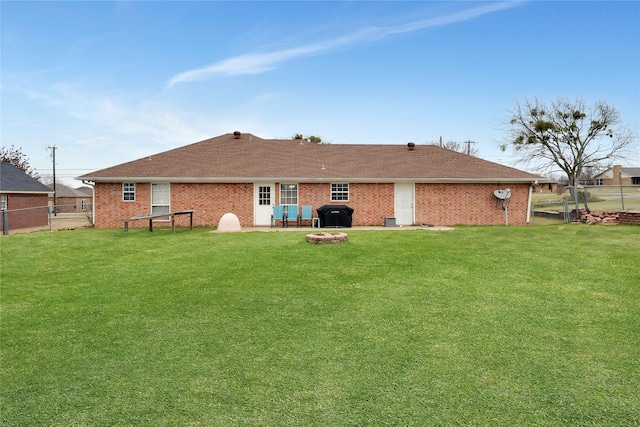 rear view of property with brick siding, a lawn, a fire pit, and fence