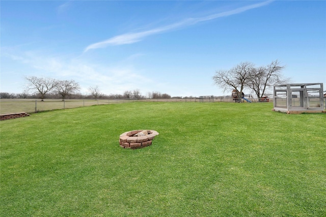 view of yard with fence, a fire pit, a playground, and a rural view