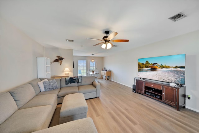 living room featuring light wood-type flooring, ceiling fan, visible vents, and baseboards