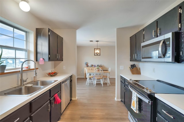 kitchen featuring stainless steel appliances, a sink, light countertops, and light wood-style floors