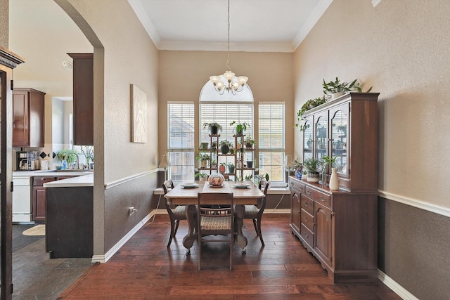 dining area with dark wood-type flooring, crown molding, baseboards, and an inviting chandelier