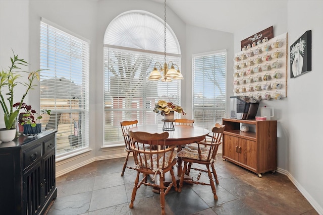 dining space featuring a chandelier, vaulted ceiling, stone tile flooring, and baseboards