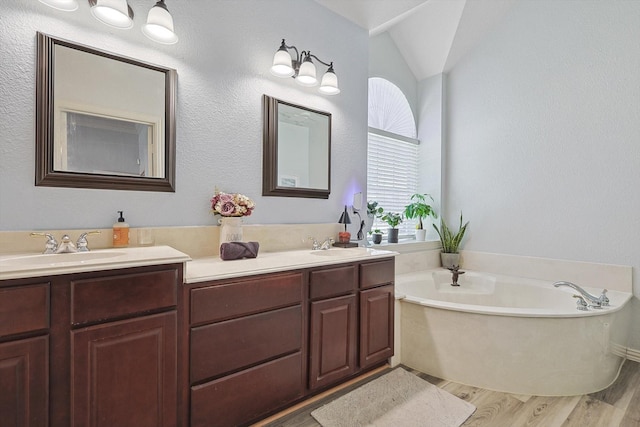 bathroom with double vanity, lofted ceiling, a sink, wood finished floors, and a bath