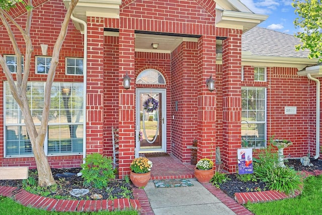 view of exterior entry featuring a shingled roof and brick siding