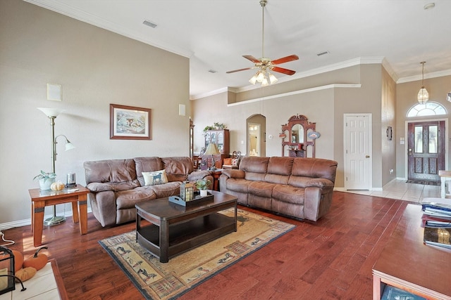 living area featuring arched walkways, wood finished floors, visible vents, baseboards, and crown molding