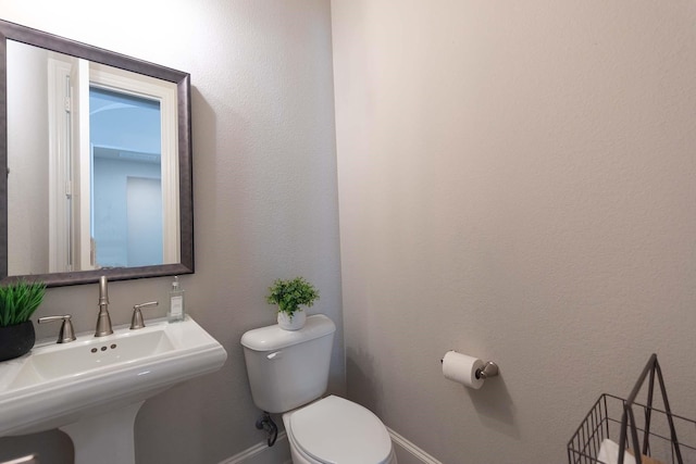 bathroom featuring toilet, baseboards, and a sink