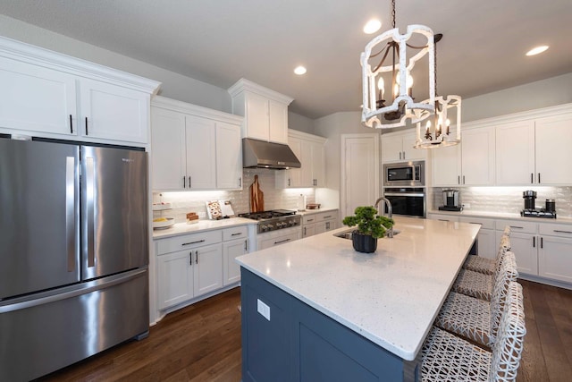 kitchen with a notable chandelier, stainless steel appliances, white cabinets, and under cabinet range hood