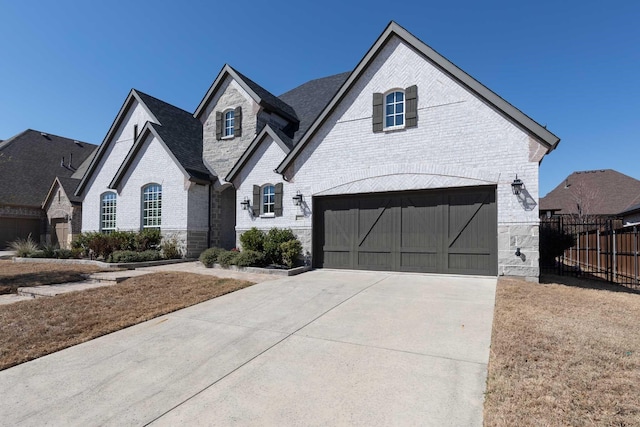 french provincial home with a garage, brick siding, fence, driveway, and stone siding