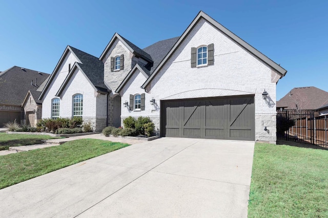 french country home featuring concrete driveway, brick siding, an attached garage, and fence